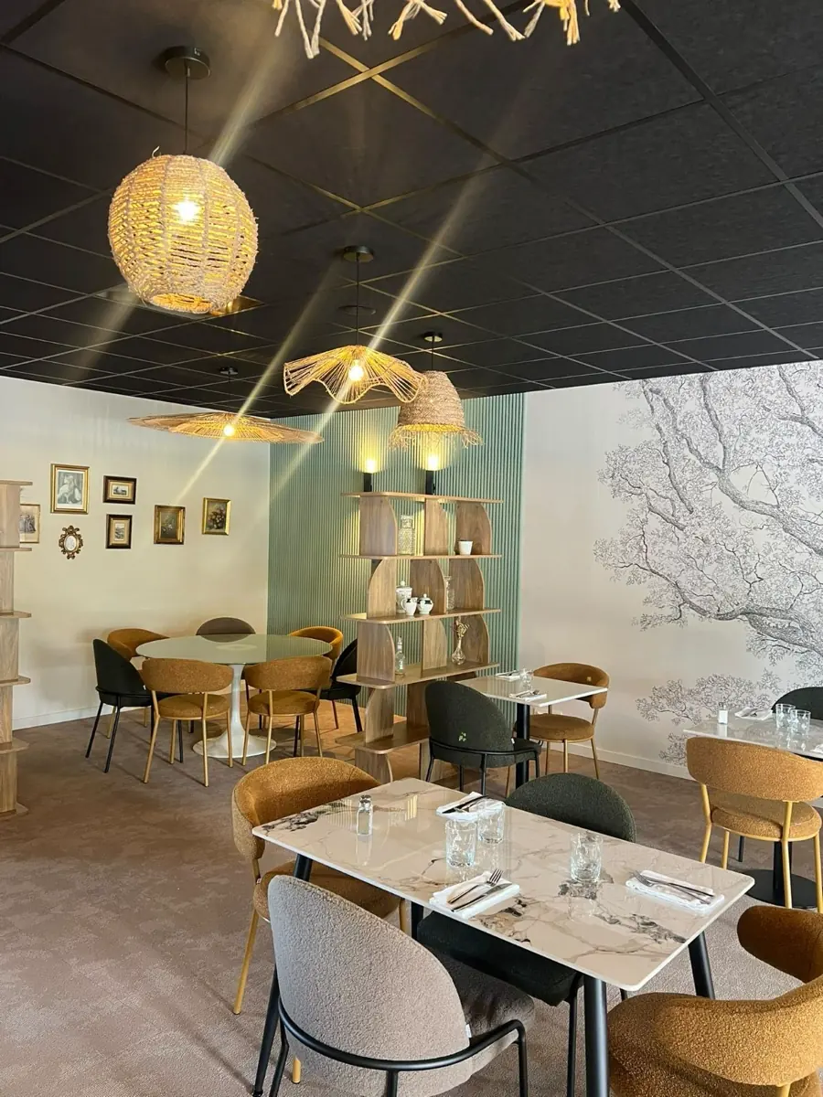 La salle du restaurant Sestra : tables en marbre clair, chaises en bouclette ocre et vert, suspensions en fibre naturelle et fresque murale représentant un arbre