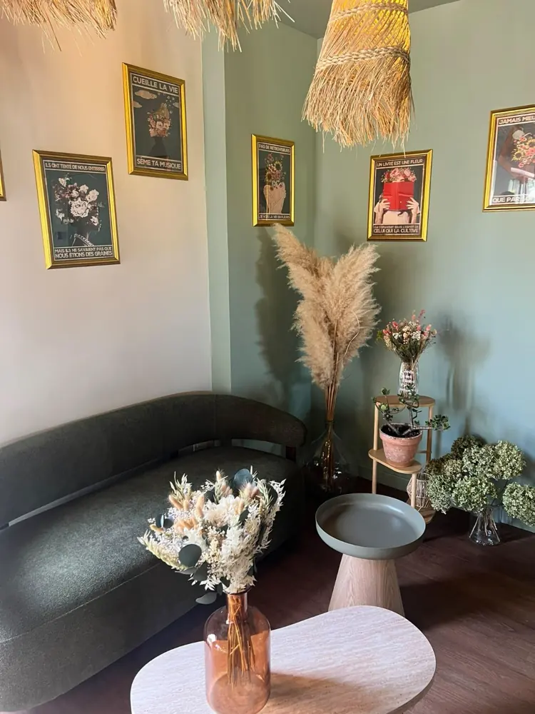 Coin salon aux murs vert amande : banquette arrondie, bouquets de fleurs séchées et affiches encadrées