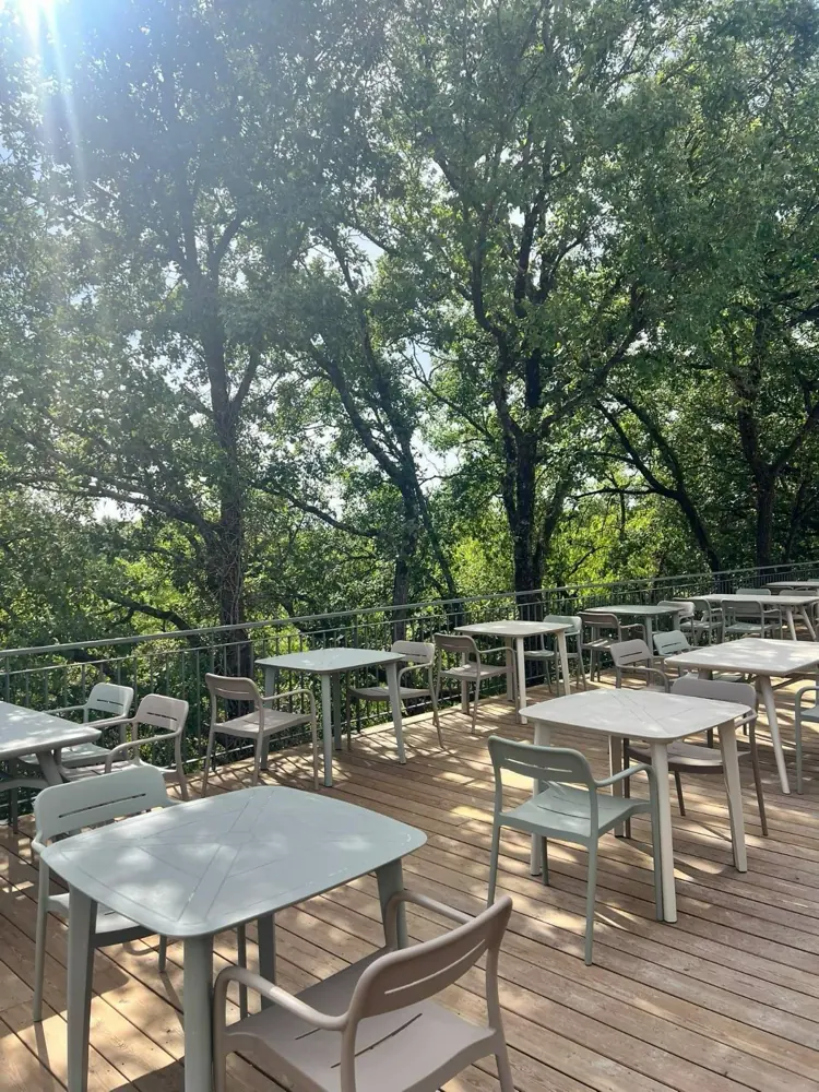 Tables et chaises vert d'eau sur la terrasse en bois, à l'ombre des chênes
